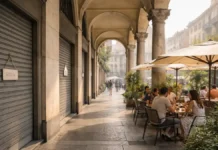 Август в Турине: почему закрываются магазины и где поесть, когда город уходит в отпуск Август в Турине: закрытые витрины магазинов и открытая летняя терраса ресторана Улица Турина в августе днем: часть витрин закрыта на отпуск, рядом открытая терраса ресторана с посетителями, летняя городская атмосфера