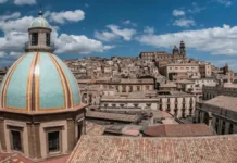 Сицилия без хайпа Case a 1 euro в Кальтаджироне: официальный перезапуск к середине 2026 Кальтаджироне перезапуск проекта «дом за 1 евро» к середине 2026 Исторический центр Кальтаджироне (Сицилия), фасады и лестницы с керамикой, на переднем плане папка «Case a 1 euro candidatura»