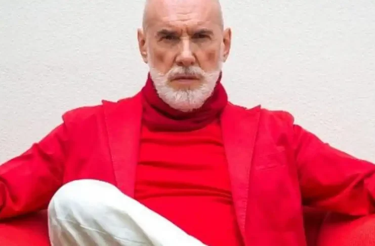 Диего Далла Пальма сидит у окна с бокалом вина, задумчивый взгляд, мягкий свет Элегантный пожилой итальянец с ухоженным лицом за столом у окна, бокал вина, атмосфера покоя и прощания.