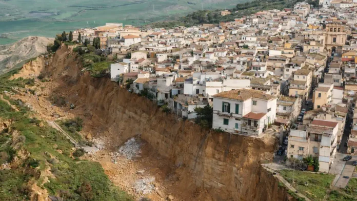 Оползень в Нискеми, Сицилия: эвакуация жителей и зона риска после непогоды итальянские спасатели и жители у ограждений «красной зоны», служебные машины на фоне, пасмурный день, ощущение организованной эвакуации и контроля безопасности